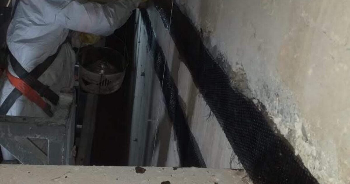 Trabalhador aplica fibra de carbono em parede de concreto