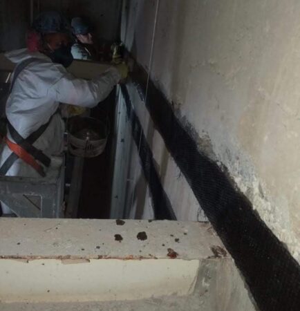Trabalhador aplica fibra de carbono em parede de concreto